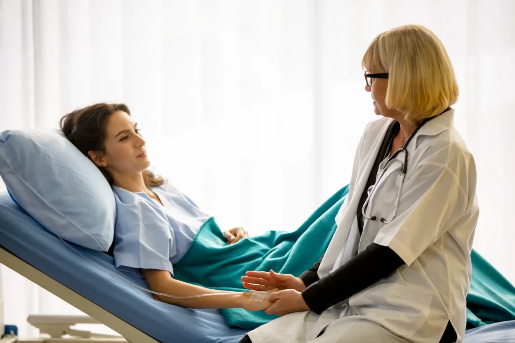 Un medico che parla alla sua paziente, seduta sul suo lettino ospedaliero.
