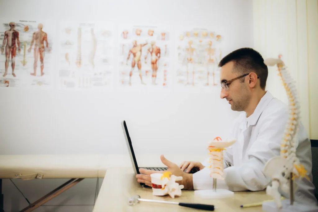 Un medico che controlla il laptop, seduto alla scrivania del suo studio.